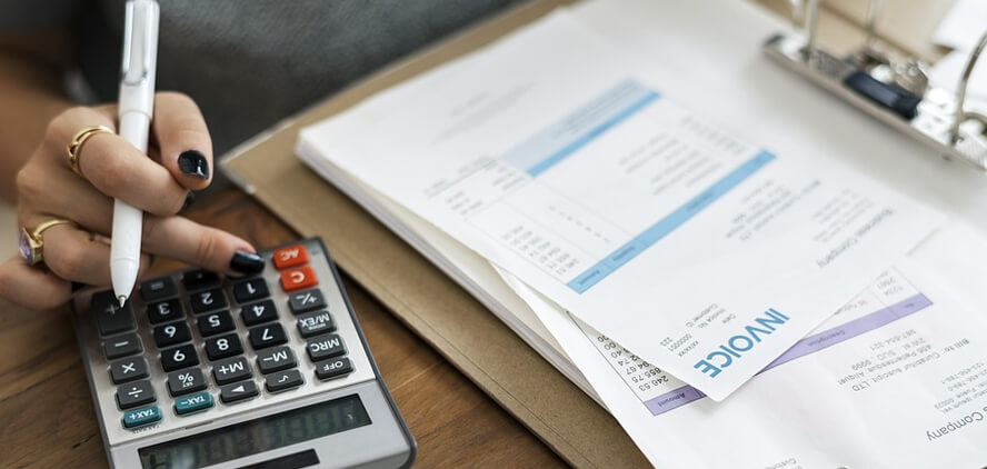person using a calculator while working with invoices and financial documents