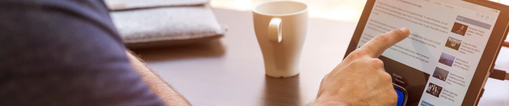 a person interacting with a tablet, likely browsing news or articles, with a coffee cup